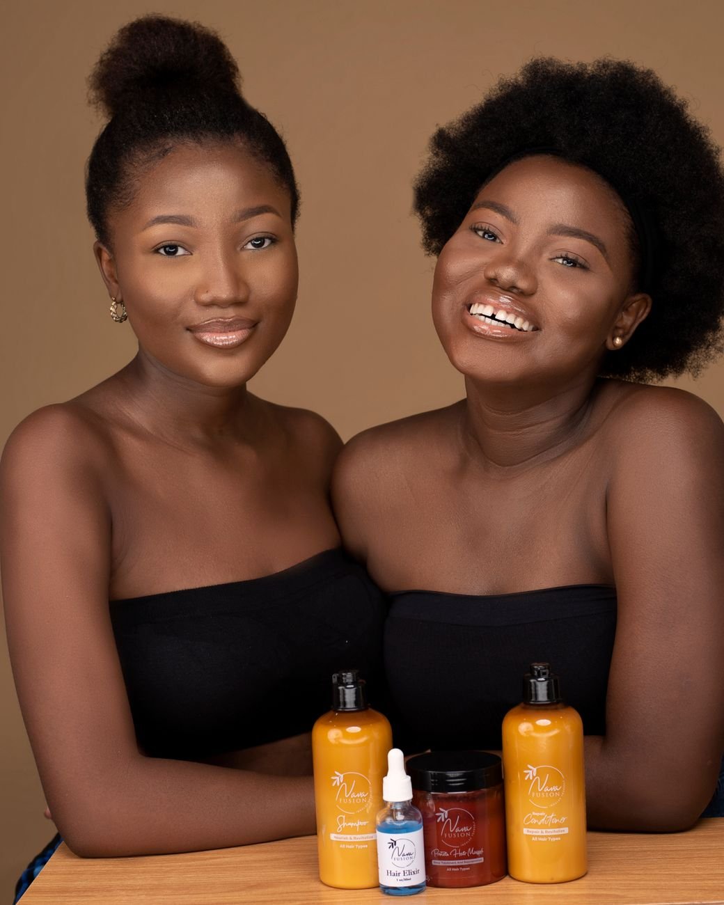 Two smiling African women promote natural skincare products in a studio setting.