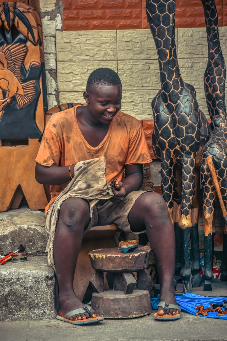 African artisan skillfully carves wooden sculptures in a vibrant outdoor market in Monrovia.