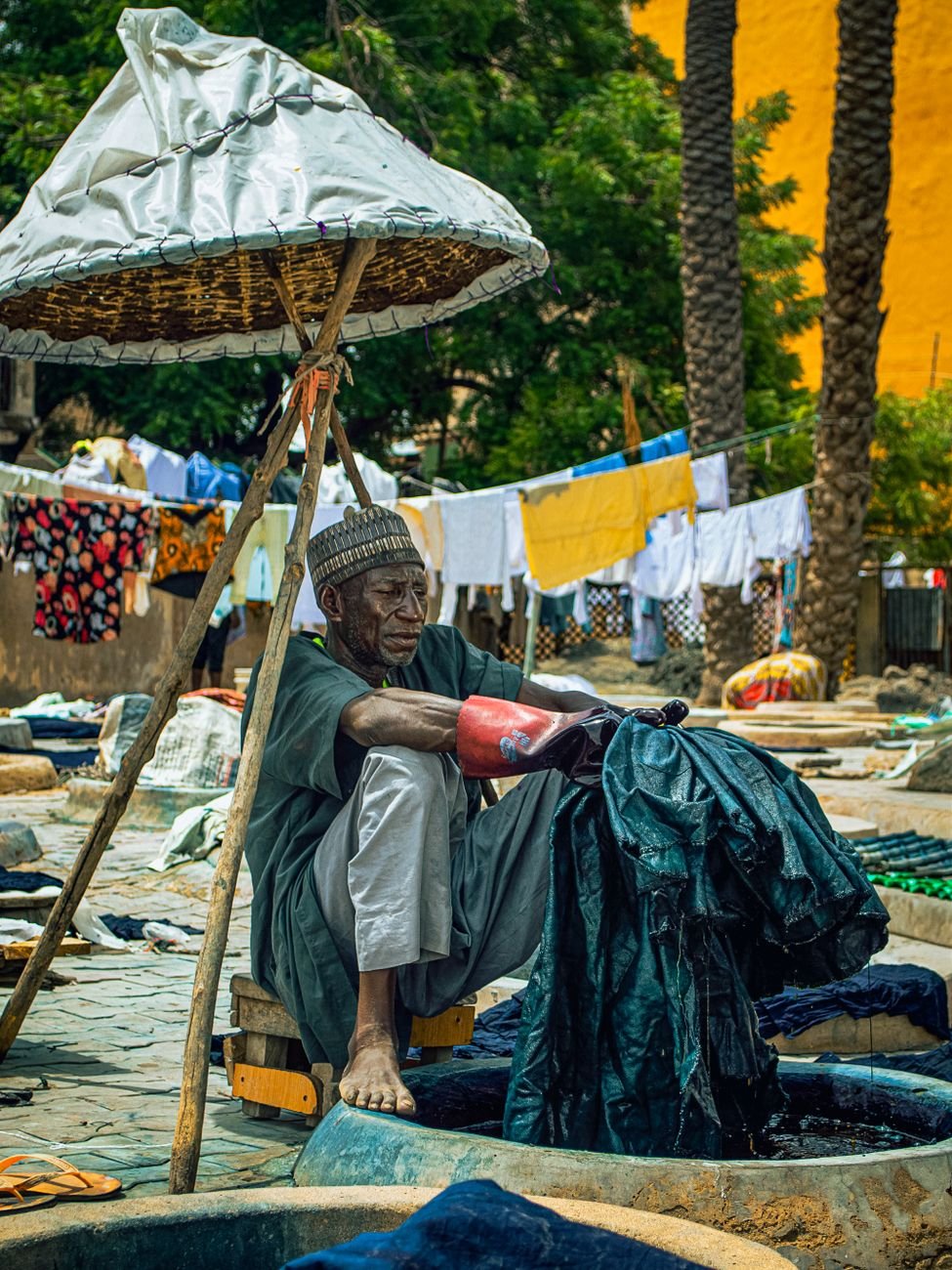 An artisan skillfully dyes fabric in an outdoor African market.